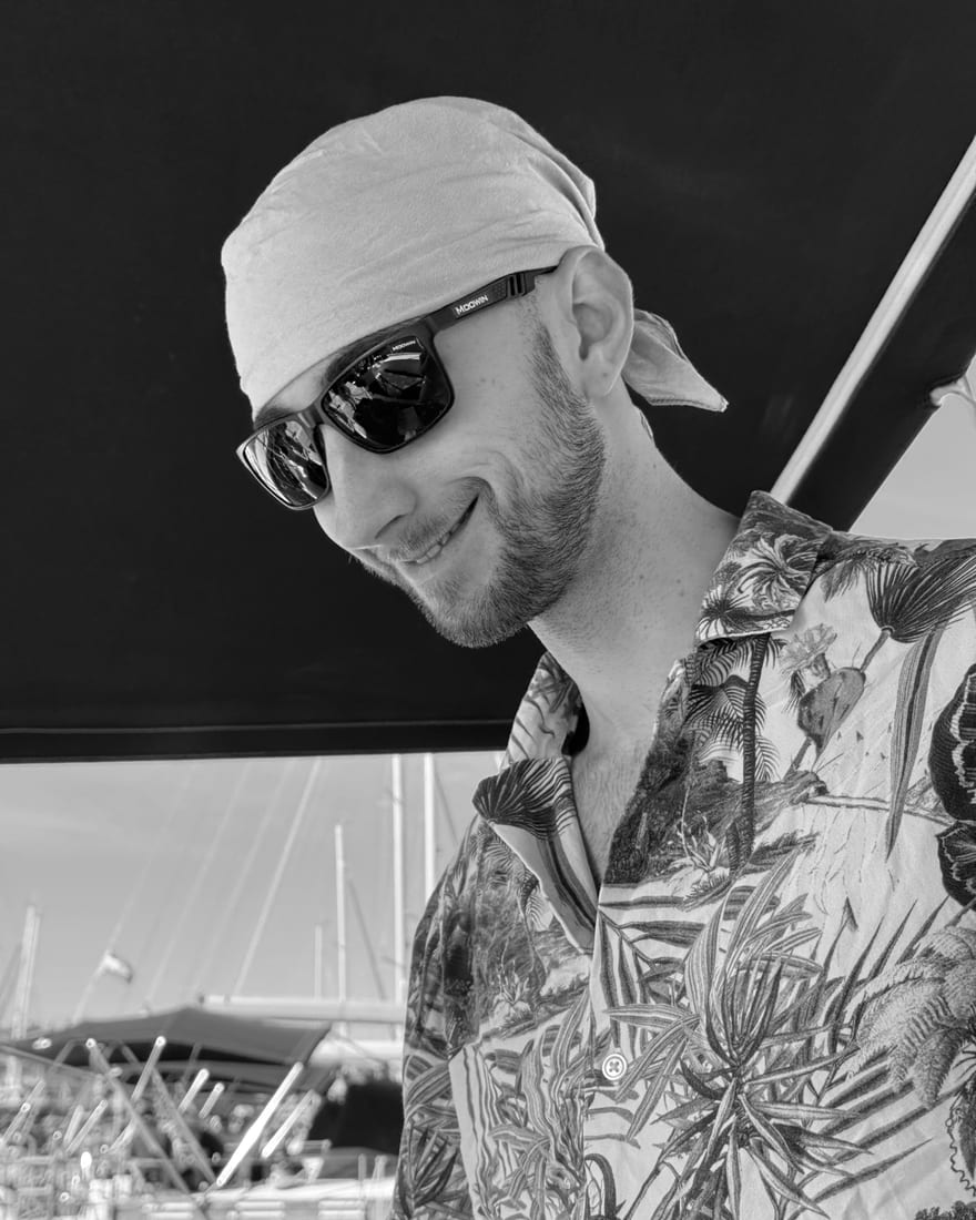 Matija Laznik on a sailboat in a bandana and sunglasses, in warm duotone